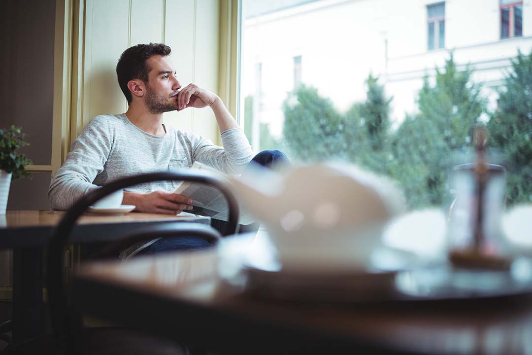 thoughtful man sitting alone cafe window light